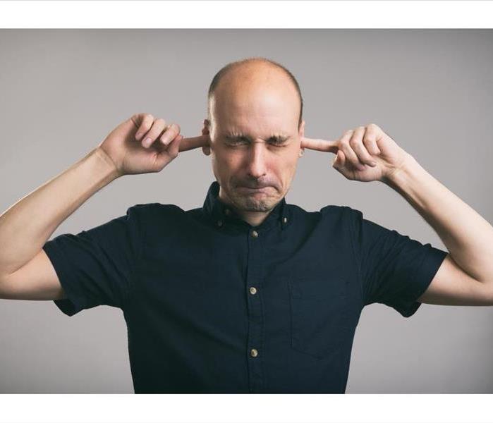 bald man covering his ears over gray background